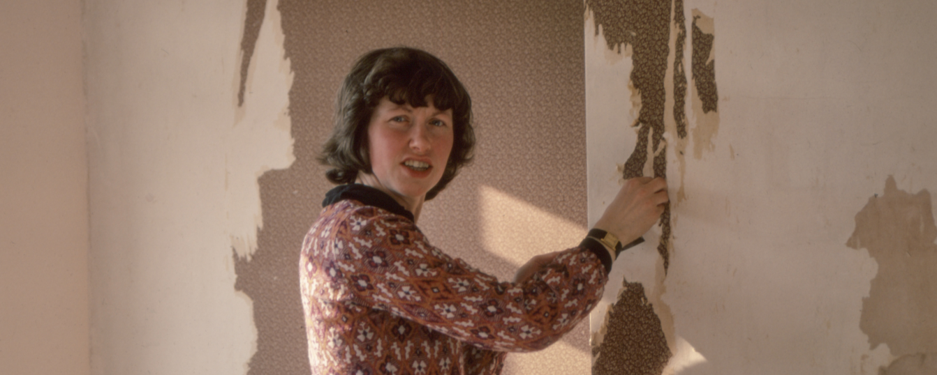 Foto de una persona mirando extrañada  ala cámara mientras qiita a pintura de una pared con su mano